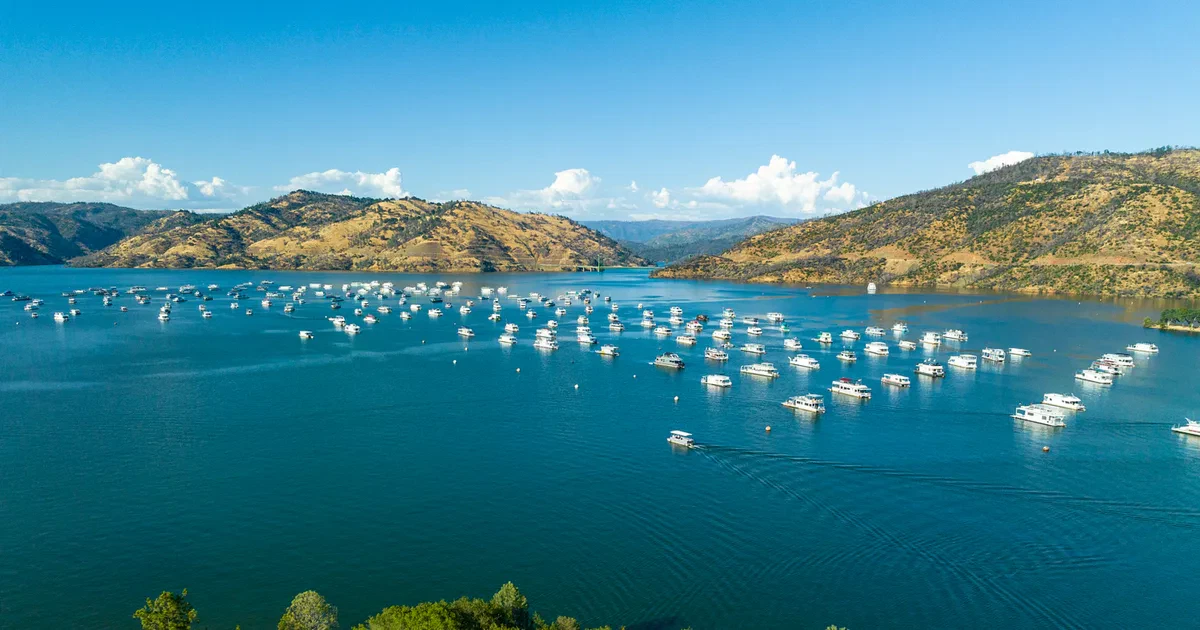 Lake Oroville_recreational lake-Oroville CA_2 Aerial view of a large lake with many boats anchored on the water, surrounded by hilly terrain under a clear blue sky.